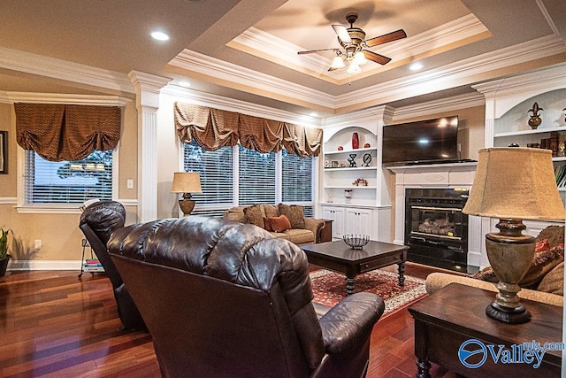 living room featuring ceiling fan, a tray ceiling, dark hardwood / wood-style flooring, and ornamental molding