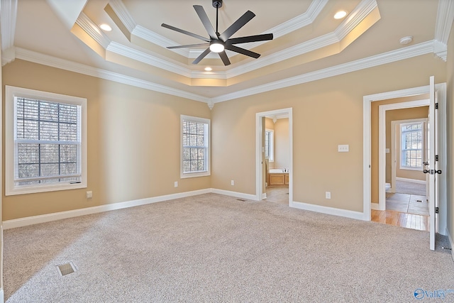 unfurnished bedroom with a raised ceiling, light colored carpet, visible vents, ornamental molding, and baseboards