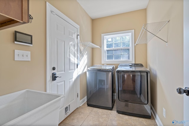 washroom featuring laundry area, baseboards, light tile patterned flooring, and washing machine and clothes dryer