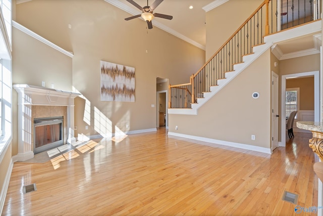 living room featuring a towering ceiling, baseboards, ornamental molding, hardwood / wood-style floors, and a tiled fireplace