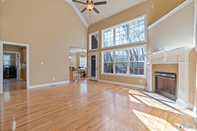 unfurnished living room with high vaulted ceiling, light wood finished floors, a fireplace, and baseboards