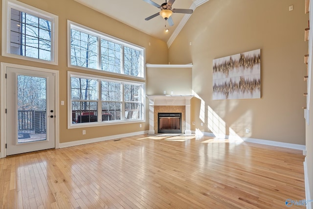 unfurnished living room featuring baseboards, a ceiling fan, a tiled fireplace, hardwood / wood-style flooring, and high vaulted ceiling