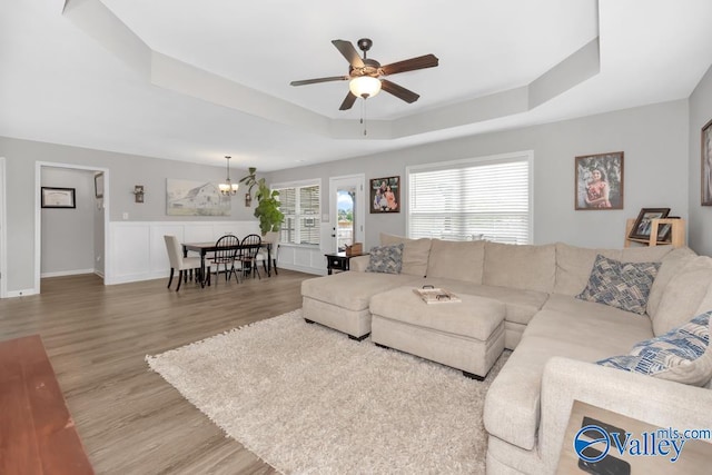 living room featuring light wood-type flooring, a tray ceiling, and ceiling fan with notable chandelier