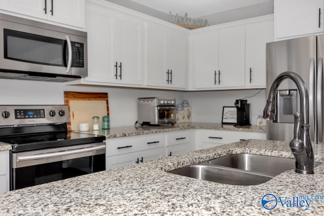 kitchen with light stone counters, stainless steel appliances, and white cabinetry