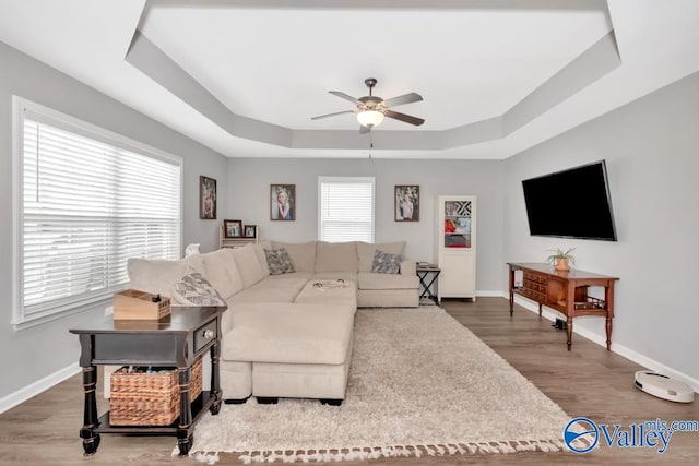 living room featuring hardwood / wood-style floors, ceiling fan, and a raised ceiling