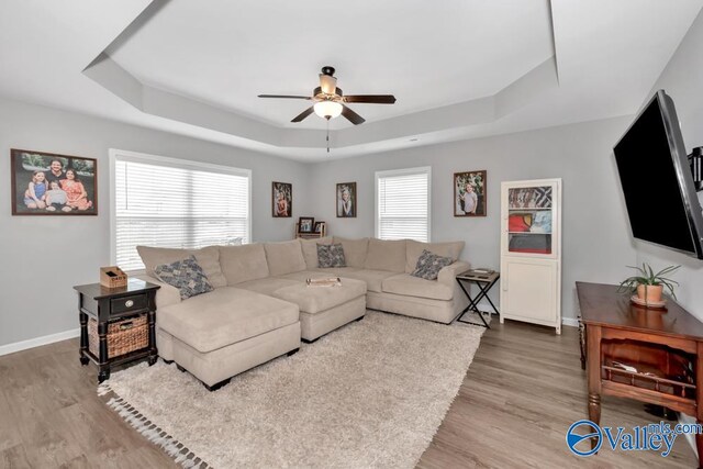 living room featuring light hardwood / wood-style flooring, a tray ceiling, and ceiling fan