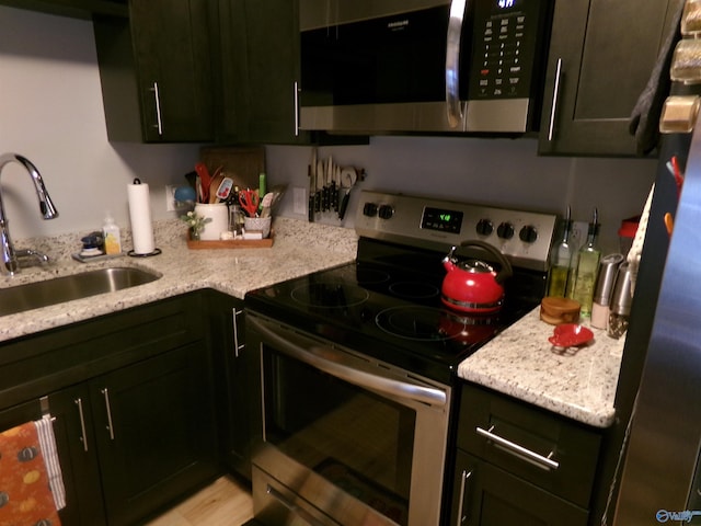 kitchen with light stone countertops, sink, appliances with stainless steel finishes, and light wood-type flooring