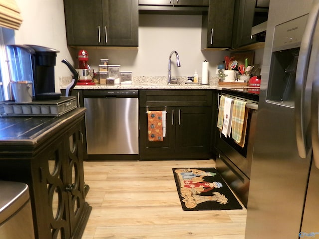 kitchen featuring sink, dark brown cabinetry, appliances with stainless steel finishes, light stone counters, and light hardwood / wood-style floors