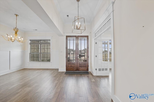 foyer entrance featuring wood-type flooring, crown molding, an inviting chandelier, and french doors