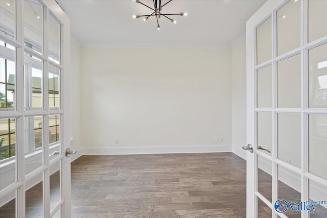 empty room featuring french doors, wood-type flooring, crown molding, and a chandelier