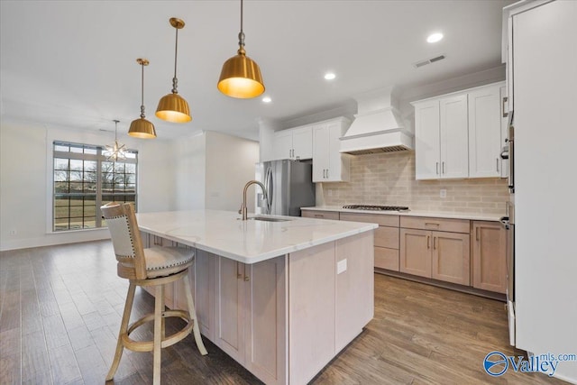 kitchen with appliances with stainless steel finishes, decorative light fixtures, an island with sink, custom exhaust hood, and light stone counters