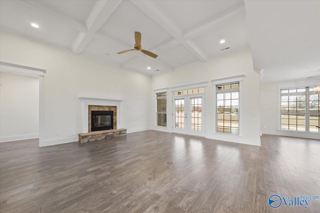 unfurnished living room featuring hardwood / wood-style flooring, a stone fireplace, coffered ceiling, and french doors