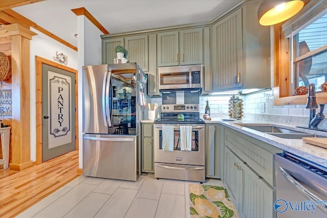 kitchen featuring tasteful backsplash, light stone counters, appliances with stainless steel finishes, green cabinets, and a sink