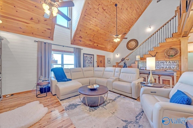 living room with stairway, ceiling fan, wooden walls, wood finished floors, and high vaulted ceiling