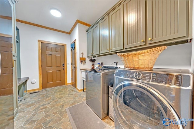 laundry room with cabinet space, baseboards, ornamental molding, washer and dryer, and stone tile flooring