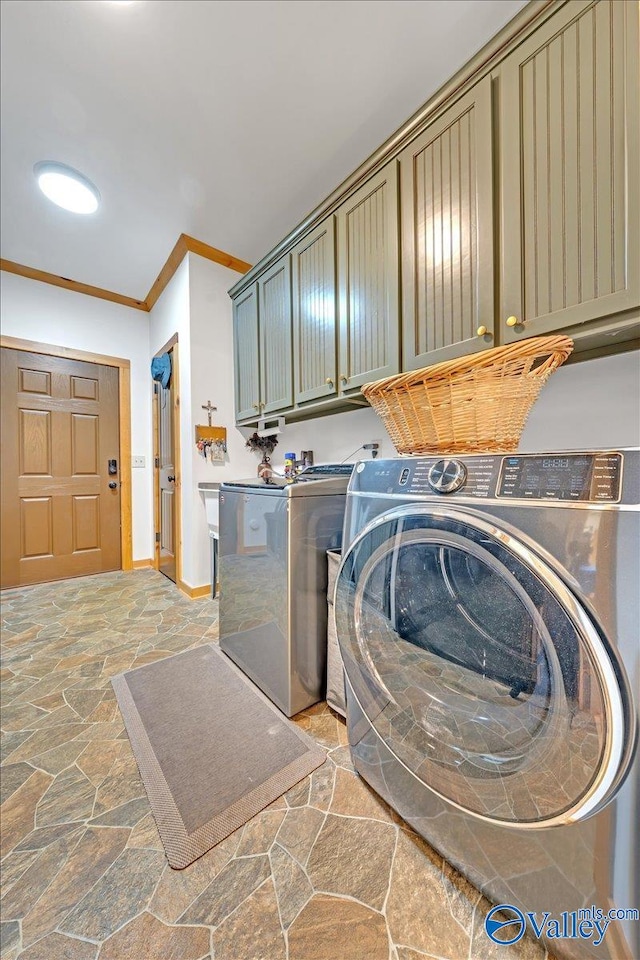 laundry room with crown molding, stone tile floors, cabinet space, washing machine and dryer, and baseboards