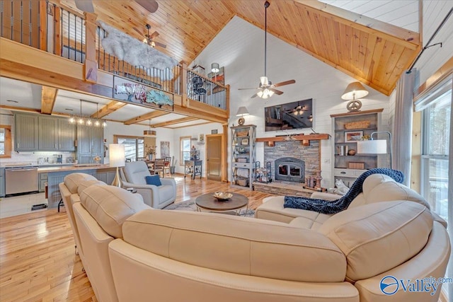 living room with wood ceiling, light wood-style flooring, a ceiling fan, and a stone fireplace