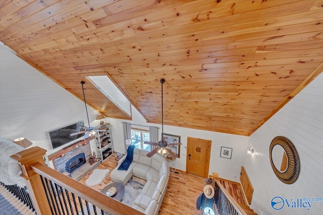 living area featuring a ceiling fan, vaulted ceiling with skylight, and wooden ceiling