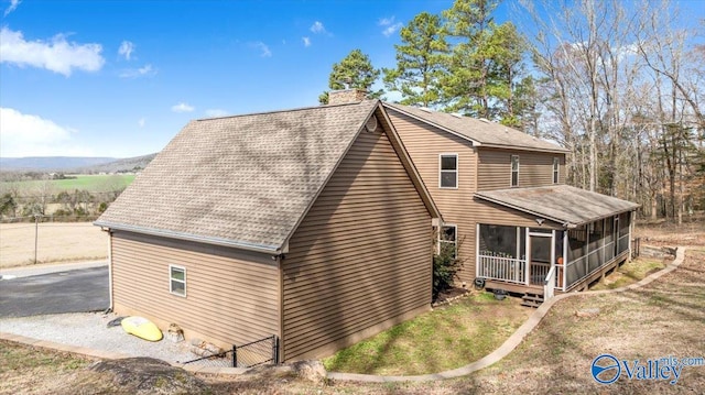 view of property exterior featuring a sunroom, roof with shingles, and a chimney