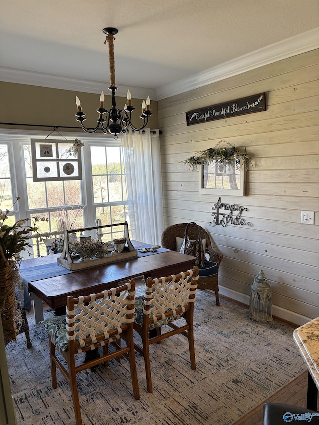 dining space featuring wood finished floors, crown molding, a notable chandelier, and wood walls