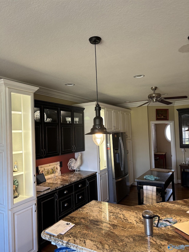 kitchen featuring light stone counters, stainless steel fridge, crown molding, and dark cabinetry