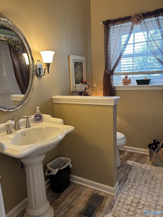 bathroom with baseboards, wood finished floors, visible vents, and toilet
