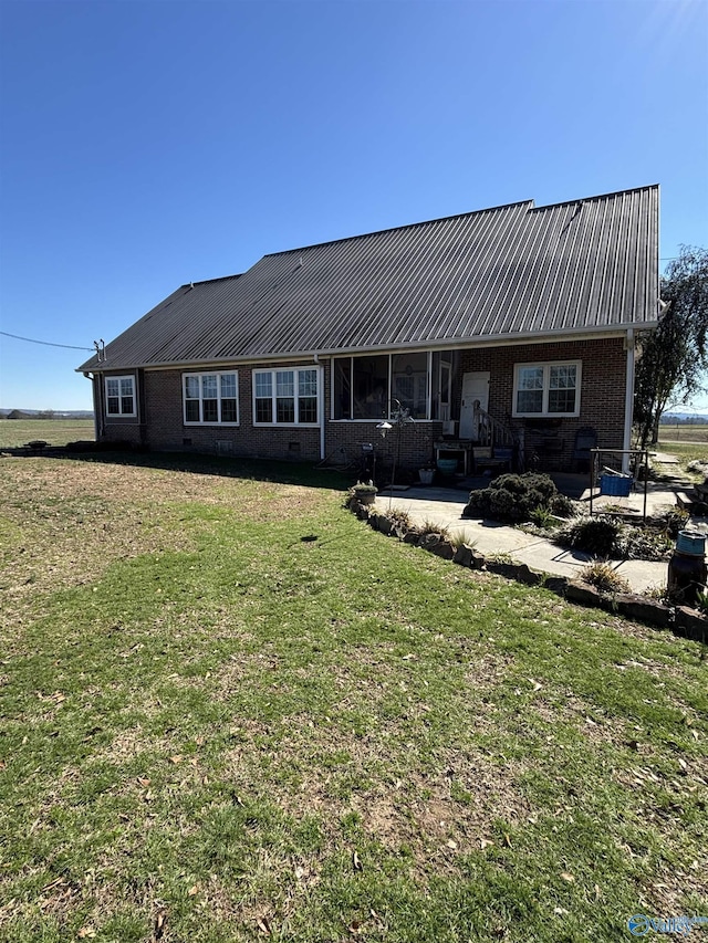 view of front of property featuring brick siding, a patio, a front lawn, and metal roof