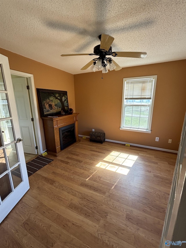 unfurnished living room featuring a fireplace, wood finished floors, a textured ceiling, and ceiling fan