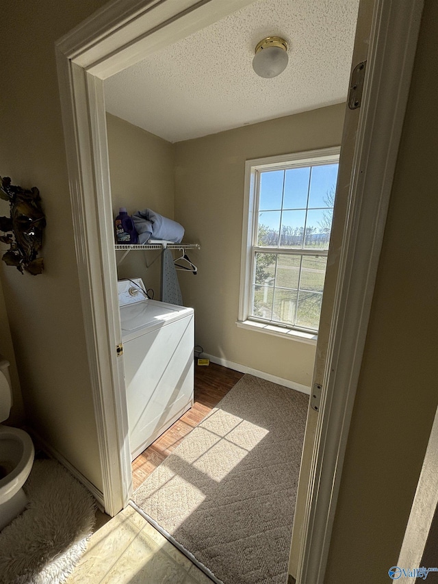 clothes washing area with baseboards, wood finished floors, a textured ceiling, and laundry area