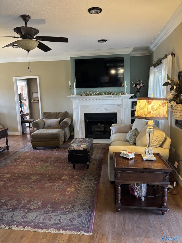 living area with a fireplace, crown molding, hardwood / wood-style floors, and a ceiling fan
