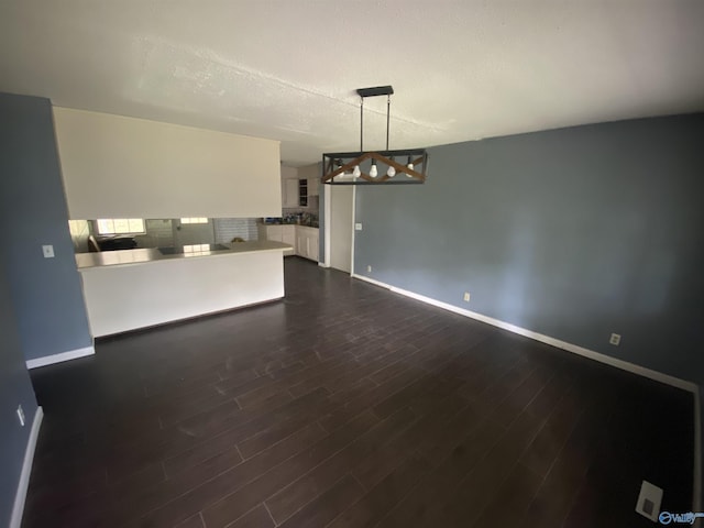 unfurnished living room with a textured ceiling, baseboards, and dark wood-type flooring