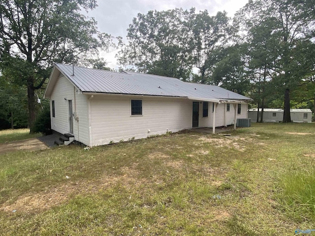 rear view of house featuring central AC unit, metal roof, and a lawn