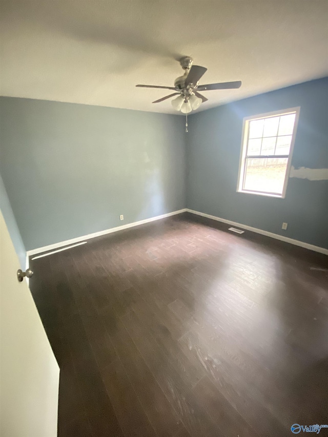 empty room with dark wood-style floors, a ceiling fan, and baseboards