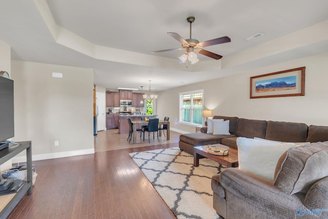 2626 SW Ashtynn Pl, Huntsville, AL 35803 - living area featuring a ceiling fan, light wood finished floors, a tray ceiling, and a chandelier