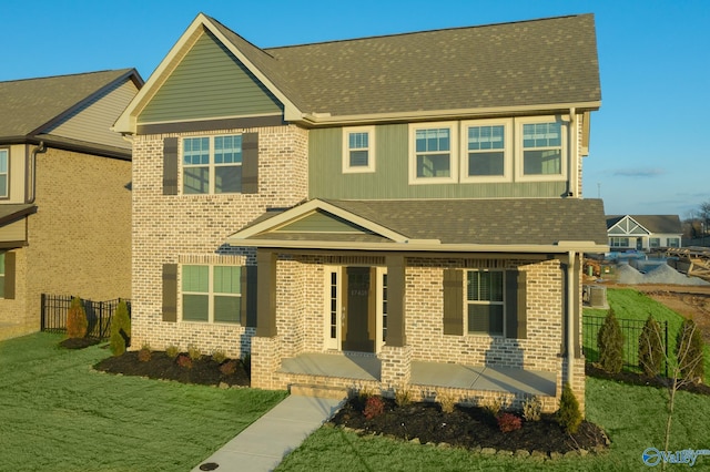 view of front of property featuring a front lawn, fence, brick siding, and roof with shingles