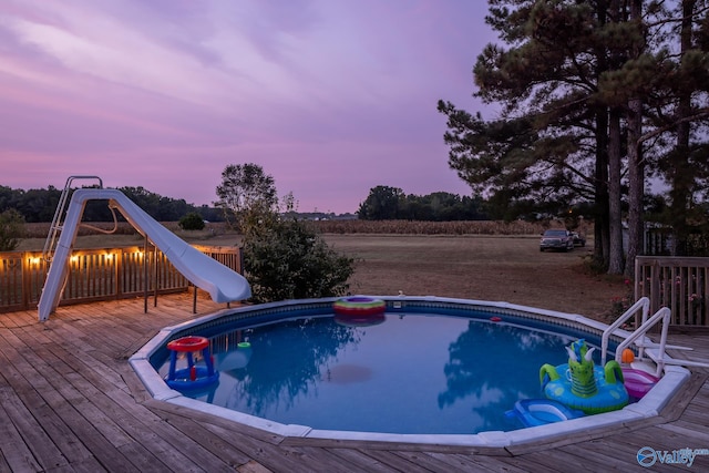 pool at dusk with a water slide and a wooden deck