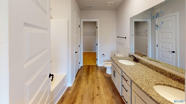 bathroom featuring dual vanity, toilet, hardwood / wood-style floors, and a bathtub