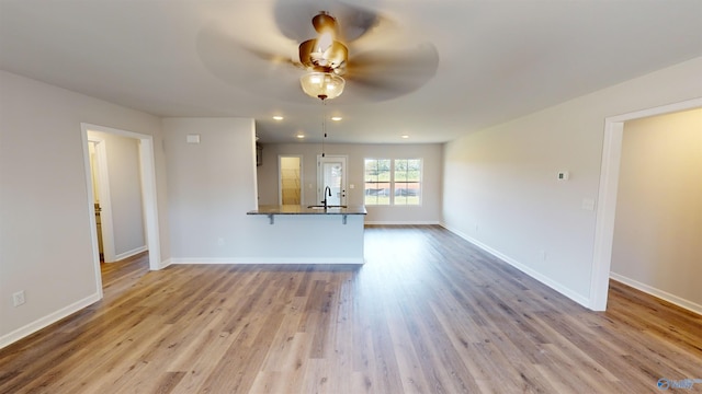 unfurnished living room featuring light hardwood / wood-style floors, sink, and ceiling fan