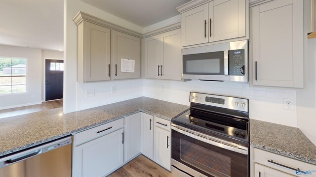 kitchen featuring decorative backsplash, light stone countertops, stainless steel appliances, and light hardwood / wood-style floors