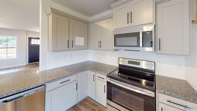 kitchen with stainless steel appliances, light wood-type flooring, light stone counters, and decorative backsplash