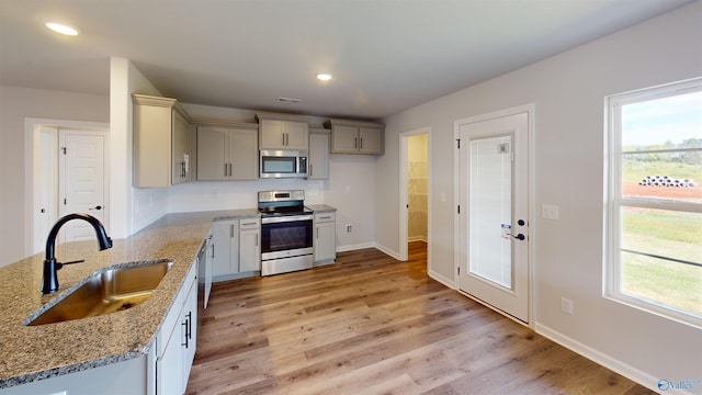 kitchen with stainless steel appliances, decorative backsplash, sink, light stone counters, and light hardwood / wood-style flooring