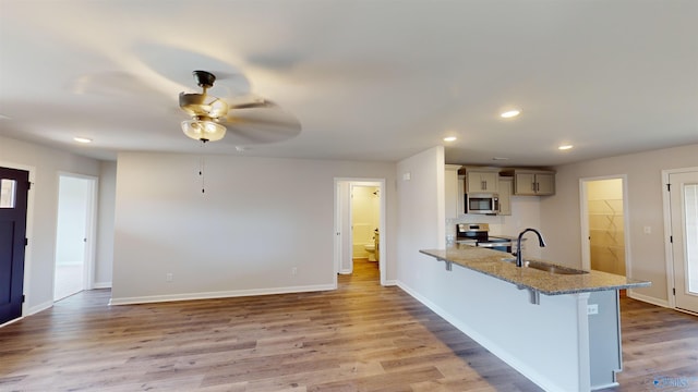 kitchen with a breakfast bar area, ceiling fan, stainless steel appliances, light hardwood / wood-style floors, and sink