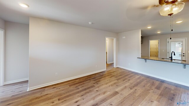 unfurnished living room with ceiling fan, sink, and light hardwood / wood-style flooring