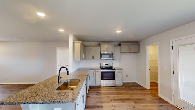 kitchen featuring appliances with stainless steel finishes, sink, light hardwood / wood-style floors, decorative backsplash, and light stone countertops