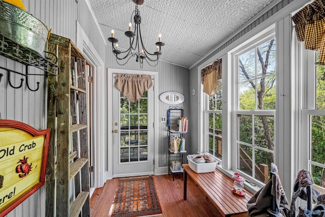 sunroom / solarium with plenty of natural light, wood finished floors, a notable chandelier, and ornamental molding