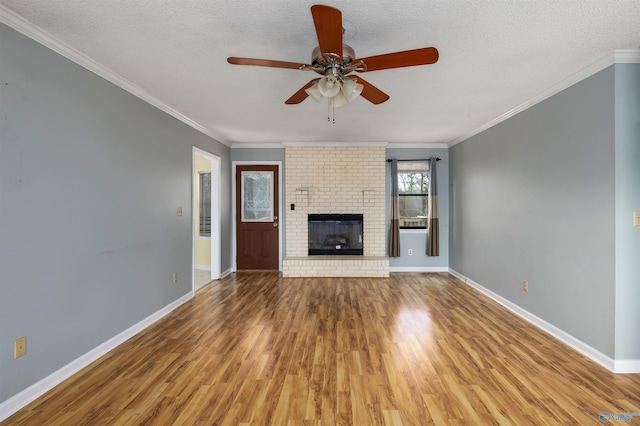 unfurnished living room featuring a textured ceiling, ornamental molding, hardwood / wood-style floors, and a brick fireplace