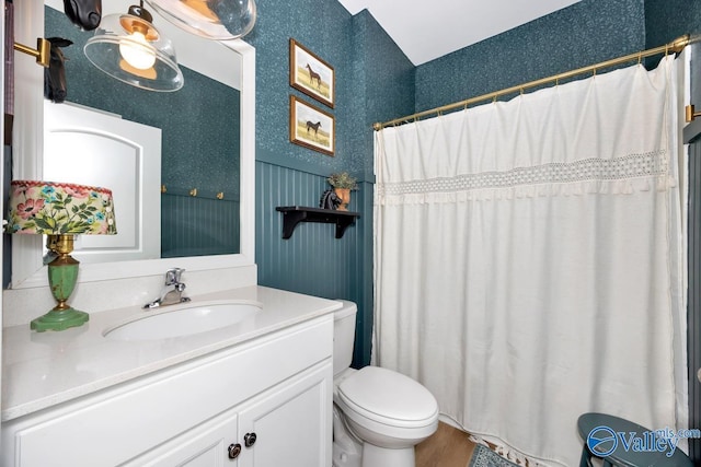 bathroom featuring toilet, wood finished floors, vanity, a shower with curtain, and wallpapered walls