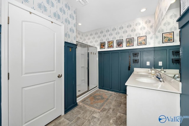 full bathroom featuring a decorative wall, a wainscoted wall, a sink, double vanity, and wallpapered walls