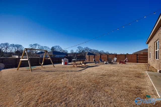 communal playground featuring a trampoline and a fenced backyard