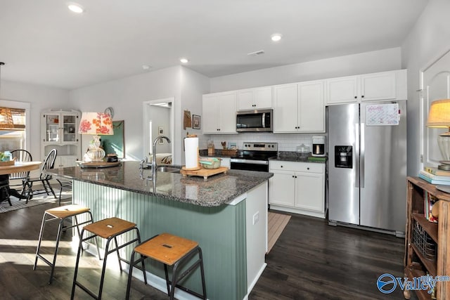 kitchen featuring dark wood-style floors, a breakfast bar area, backsplash, appliances with stainless steel finishes, and a sink